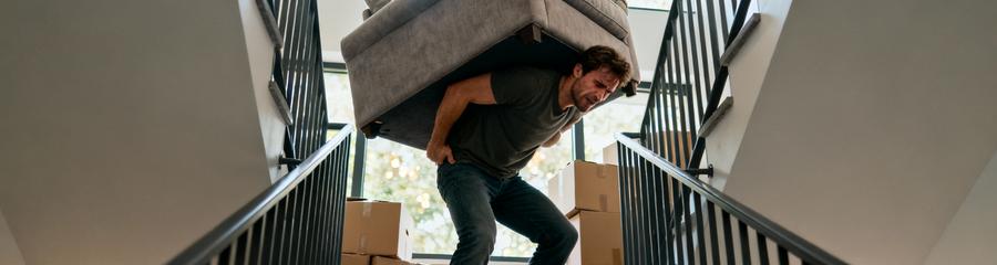 Homme transportant seul canapé dans escalier, effort intense et posture dangereuse lors déménagement solo