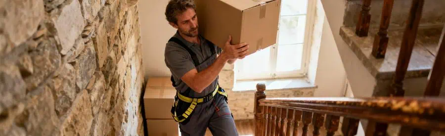 Déménageur professionnel portant carton dans escalier maison lotoise, geste technique maîtrisé