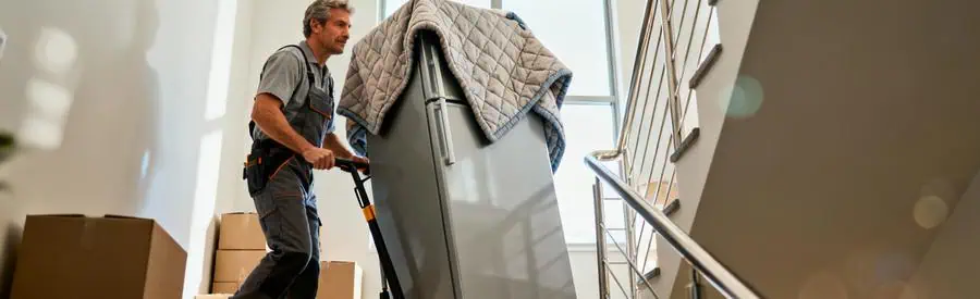 Déménageur professionnel transportant réfrigérateur protégé dans escalier avec diable, geste maîtrisé